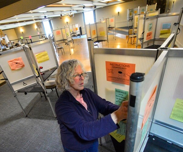 a woman puts paper instructions up in a voting booth