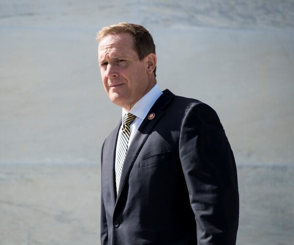 ted budd in a black suit and striped tie walking