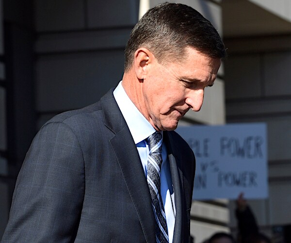 michael flynn walks outside with his head down and protest placards in the background