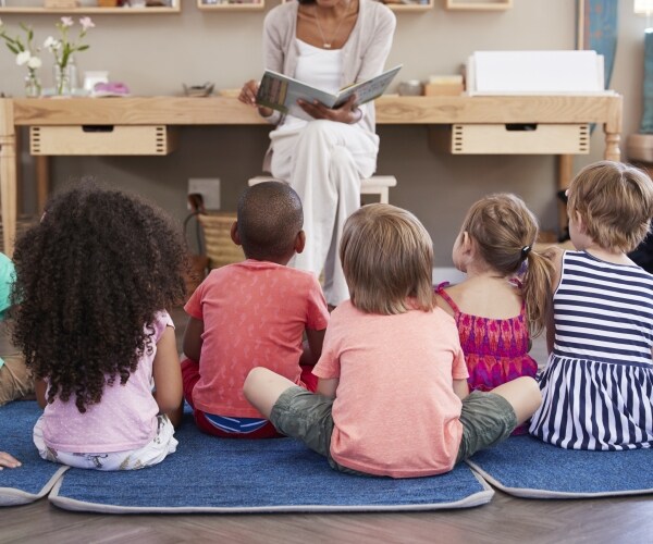 children sit on the floor as a teacher reads to them