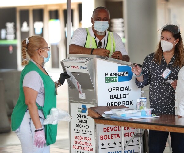 poll workers wearing masks while a voter puts her ballot in the box