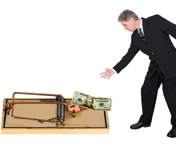 businessman reaches for money in a mouse trap.