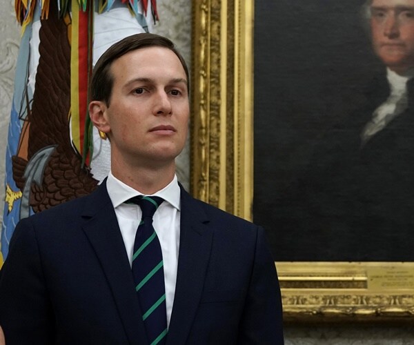 jared kushner stands against a wall and listens to others speak.