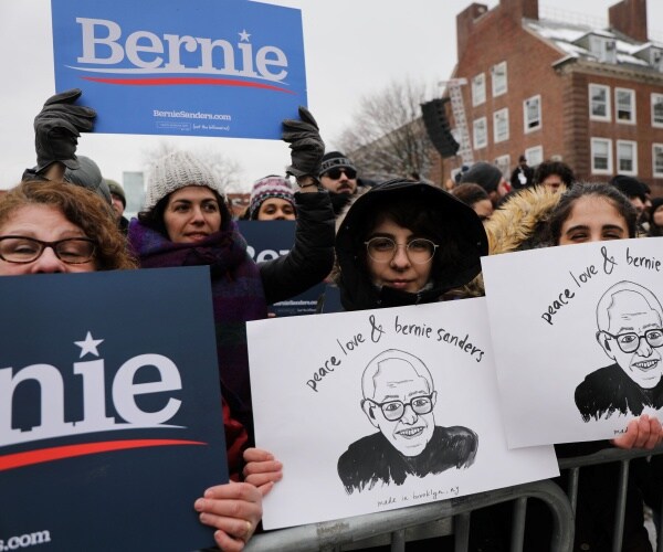 bernie sanders rally with supporters wearing coats and hats holding up signs in support