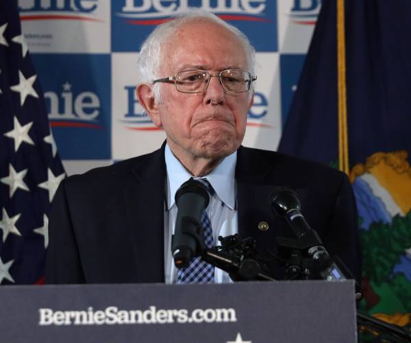 bernie sanders fowns as he stands behind a podium