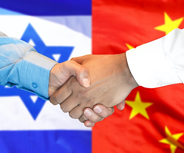 a man in front of an israeli flag shakes another man's hand in front of a chinese flag