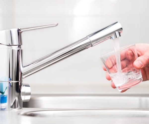 person getting water from tap into a glass