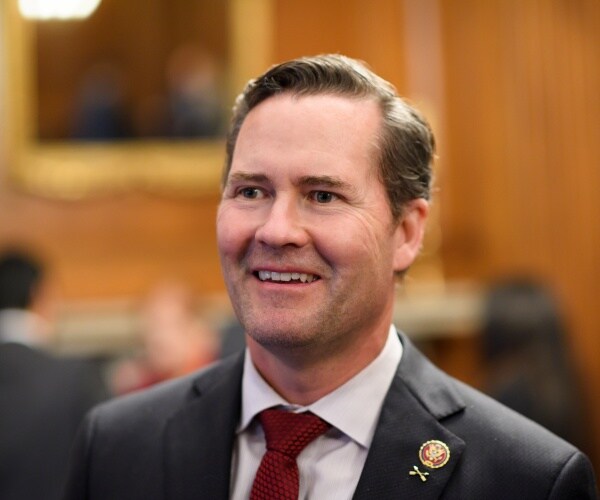 michael waltz in a black suit and burgundy tie smiling