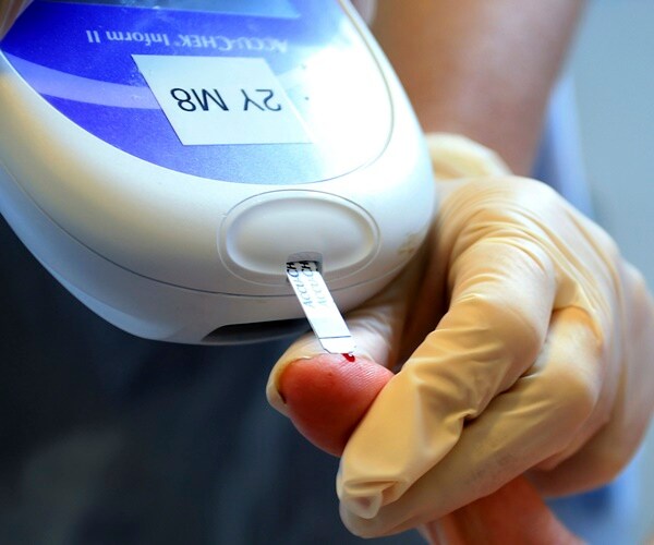 a healthcare practitioner takes a blood sample from a patient's finger