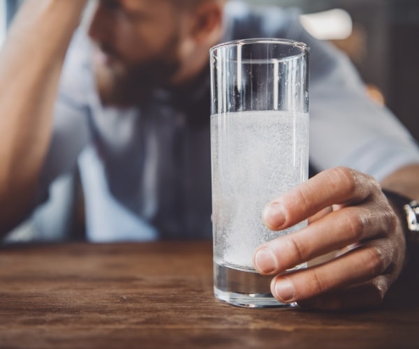 man with head in hand, holding onto water with alka-seltzer to relieve a hangover
