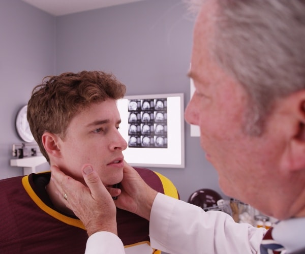 doctor examining neck of football player, with brain images on the lightbox