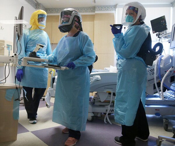 medical workers look at a monitor in the room of a coronavirus patient in a hospital