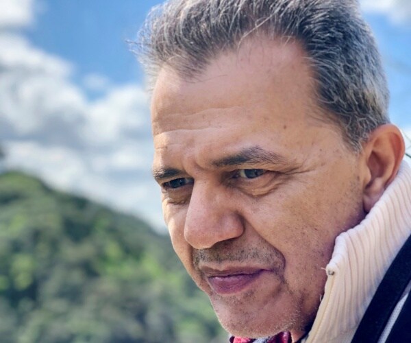 sharmahd in a white sweater and jacket with clouds and mountains in the background