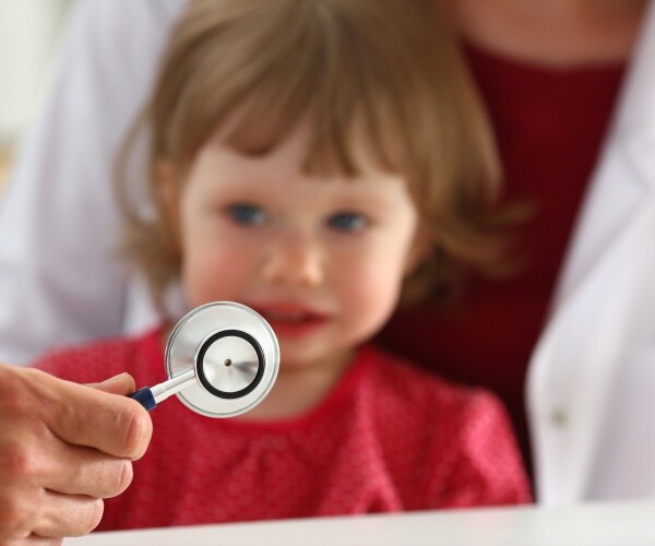 young child being held by parent looking scared at healthcare worker with stethoscope