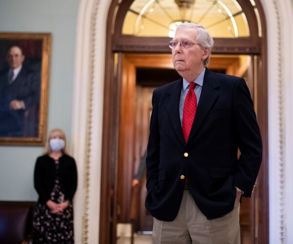 mitch mcconnell in a red tie and black blazer standing with a woman wearing a face mask in the background