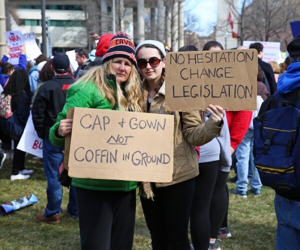 women holding signs at a rally "cap & gown, not coffin in ground"