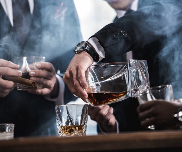 three men in suits smoking cigars and drinking bourbon
