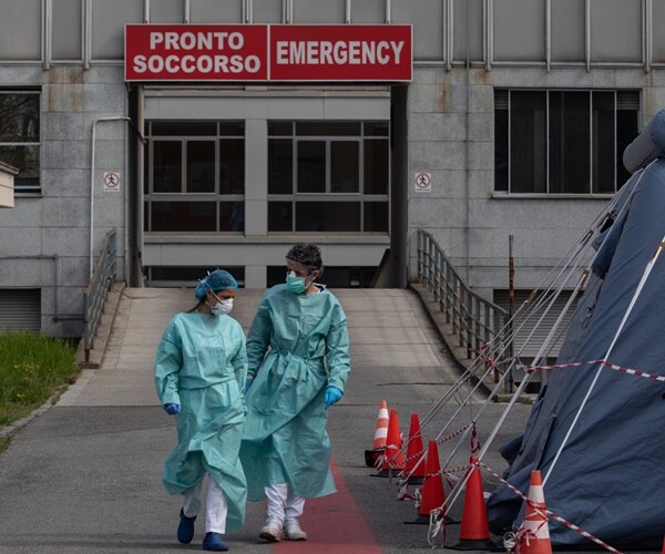 italian nurses in full protective gear walk outside a triage tent  in milan