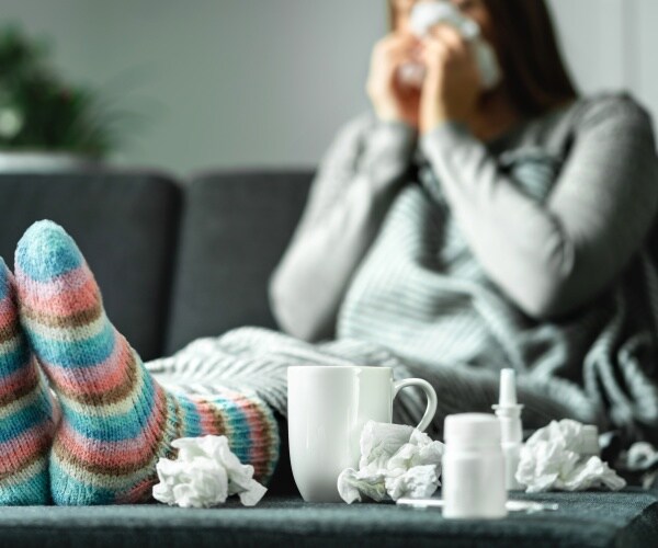 woman sick on couch blowing nose with lots of tissues around