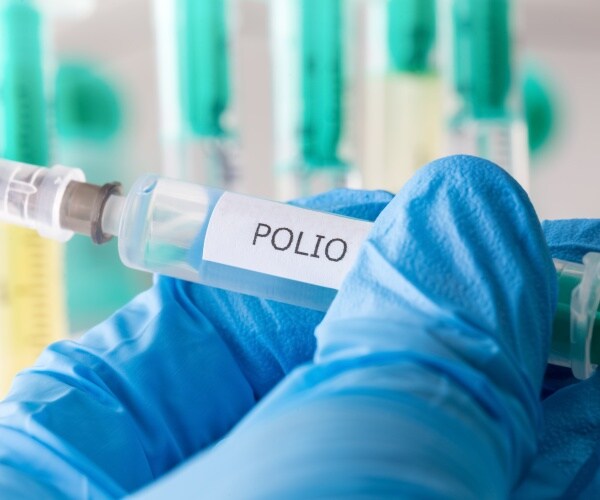 closeup of gloved hand holding syringe with polio vaccine