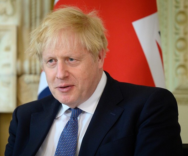 boris johnson sits in front of flag