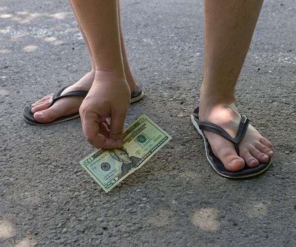 person wearing flip flops picks up a 20 dollar bill on the road
