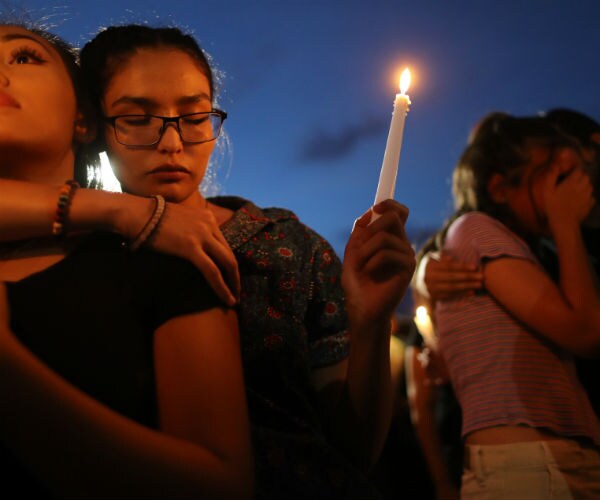young hispanic women at a memorial hold a candle and cry