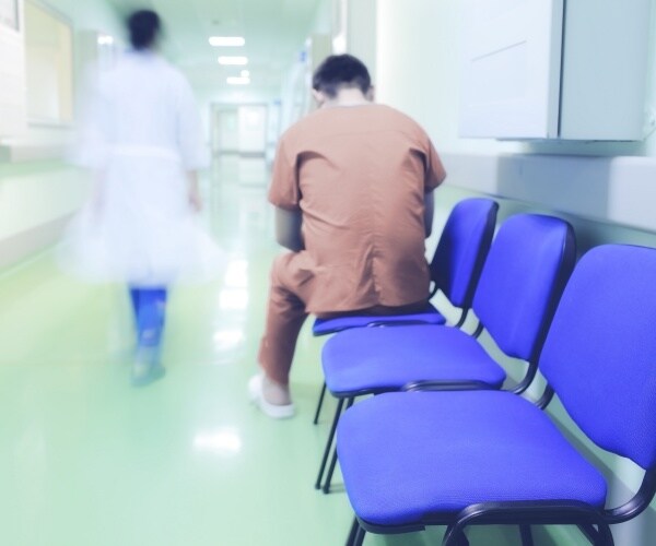 hospital patient in hall of hospital and out-of-focus healthcare worker walking by