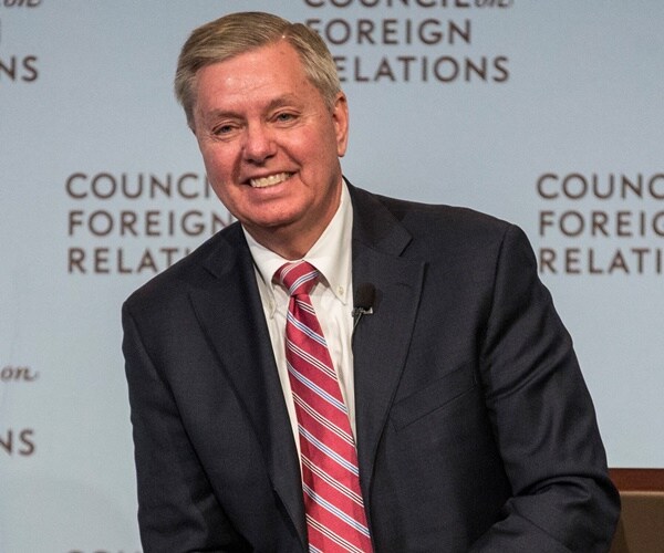 lindsey graham sits on stage and smiles
