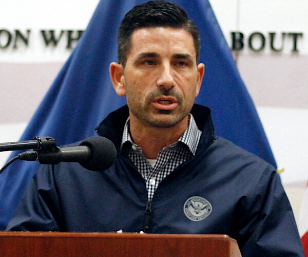 chad wolf stands behind a podium at a news conference