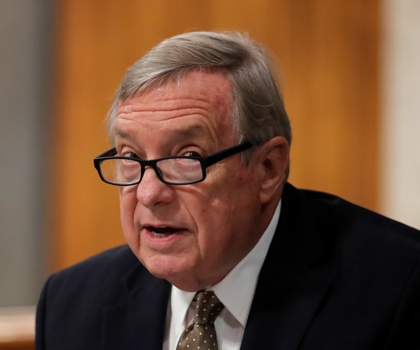 durbin in a suit and polka dotted tie wearing glasses