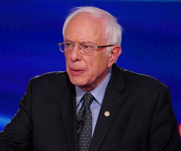 sanders in a black suit and blue shirt on the debate stage