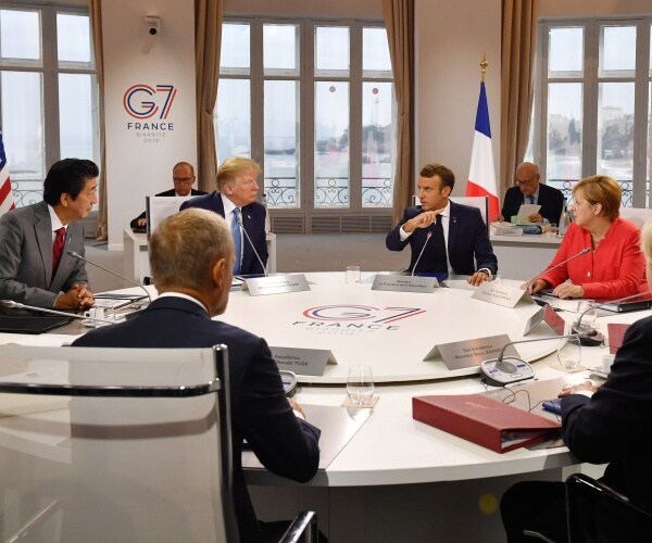 world leaders sit at a circular table at the g7 summit; trump, abe, donald tusk, macron, and merkel are shown