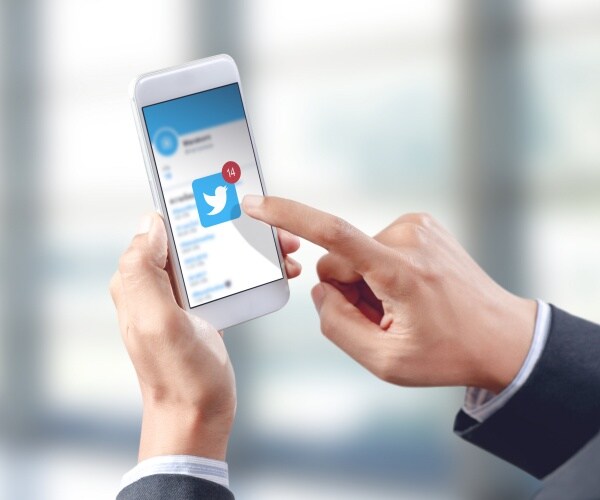 person holding up a smart phone with the twitter icon