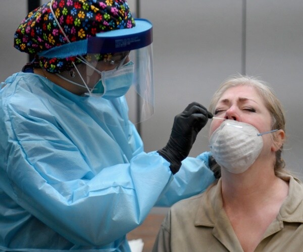 nurse in blue protective suit takes a nasal swab of a woman to test for covid