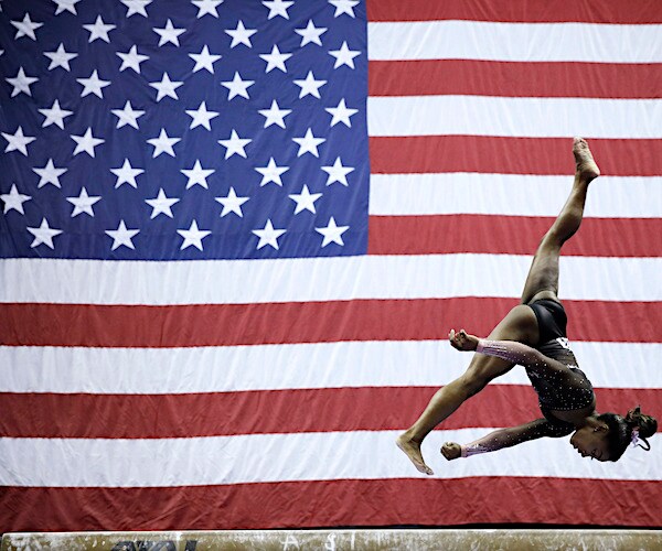 olympic gymnast simone biles flips in a routine with a large american flag in the background