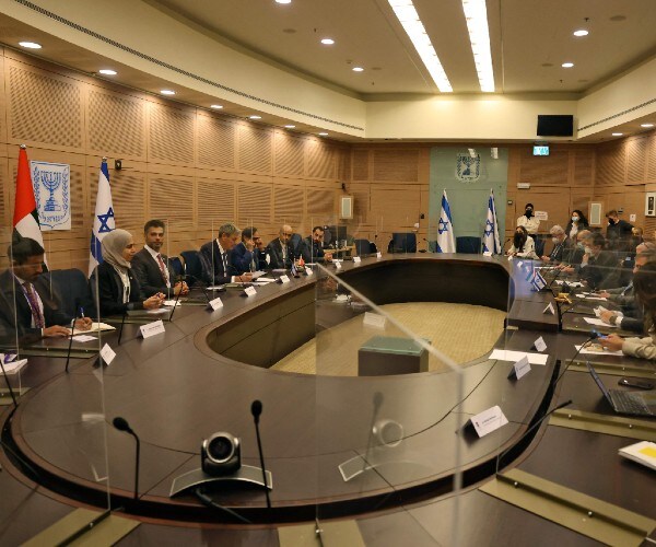 officials seated around a large table with israeli and emerati flags