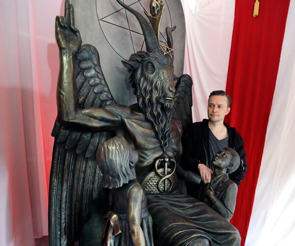 a man stands next to a nine-foot statue of a goat-headed idol