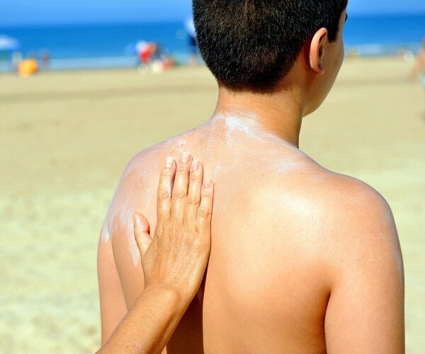 woman applying sunblock to young boys back