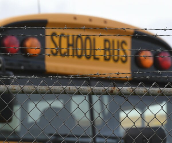 the top of a school bus is seen behind a wire fence