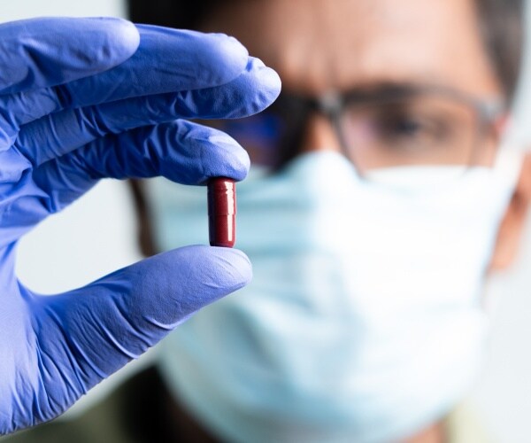 Doctor with gloved hands holds up Merck COVID pill