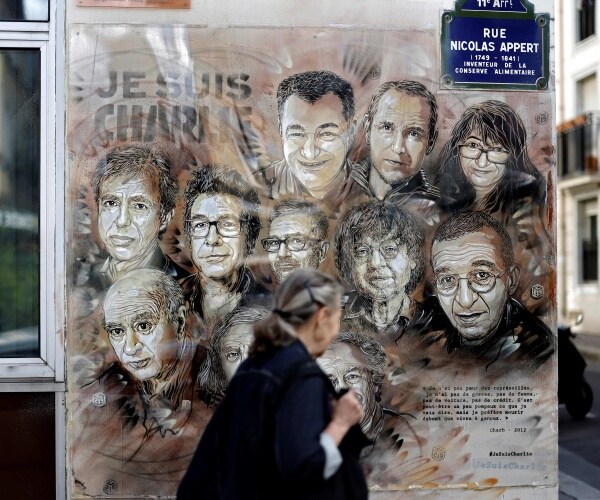 woman walks by a painting with faces of those killed in attack on charlie hebdo in 2015