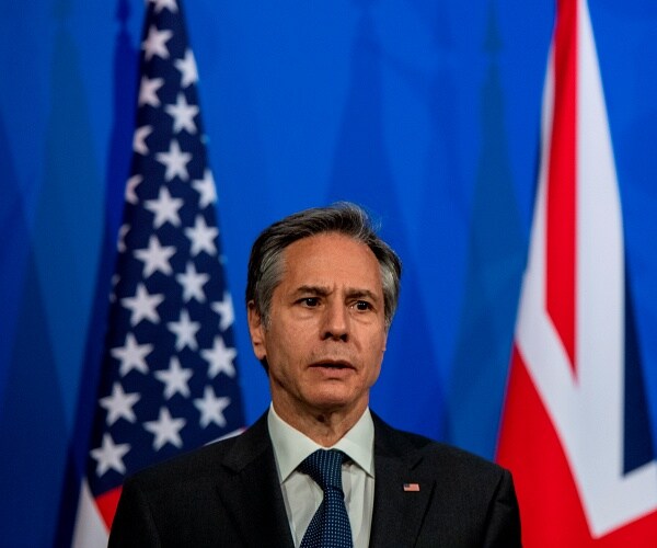 antony blinken stands in front of us and uk flags