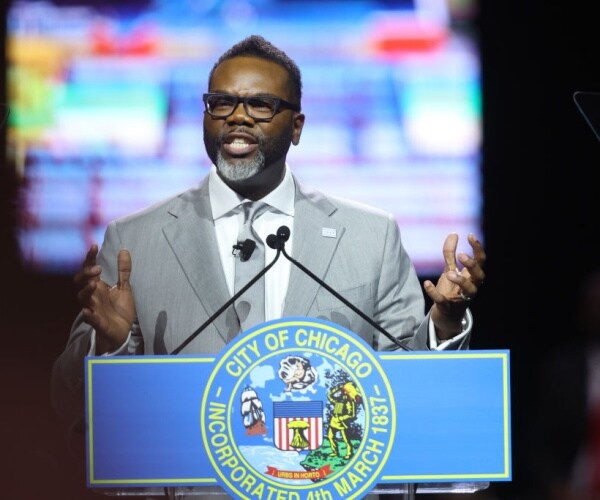 chicago mayor brandon johnson gestures behind podium with blue city of chicago sign