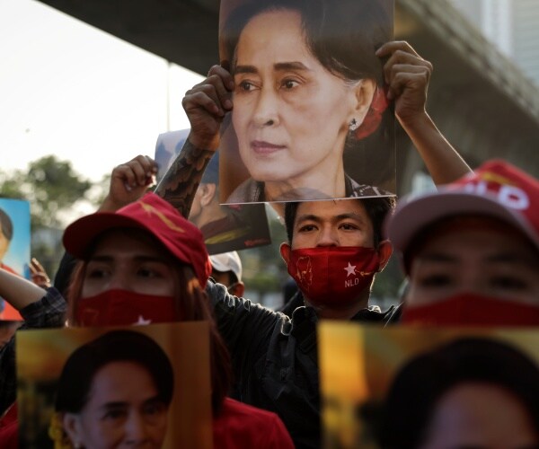 protesters wear red face masks and hold up posters of suu kyi