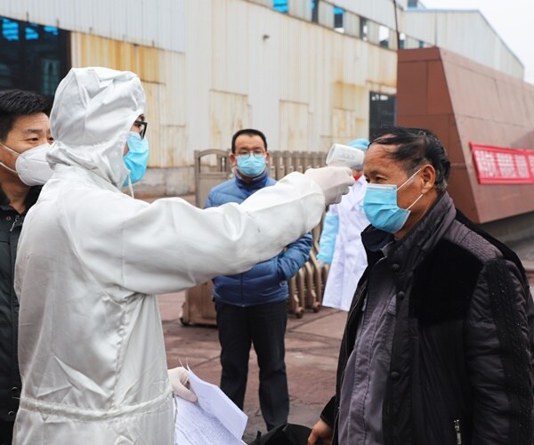 a chinese migrant has his temperature taken by a worker in a medical gown and mask