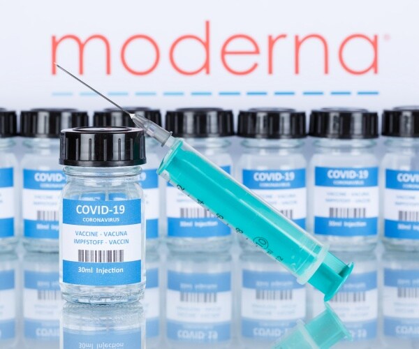 Moderna logo behind Moderna vials of COVID vaccine