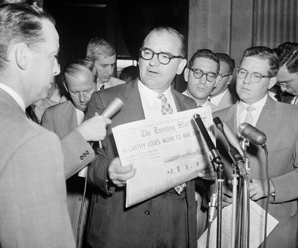 Joseph McCarthy holds a newspaper as he is interviewed during a news conference