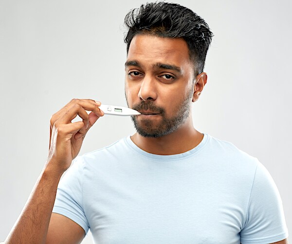 a man looks solemn as he takes his own temperature with a digital thermometer