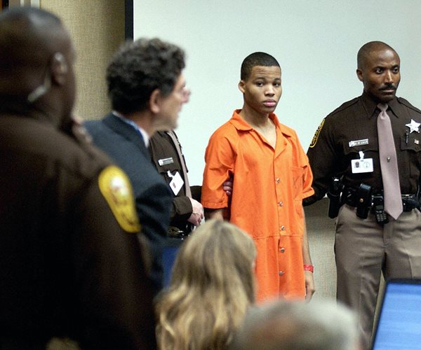 lee boyd malvo wearing an orange jail jumpsuit as he stands in a courtroom